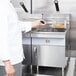 A person in a white coat using a Cooking Performance Group countertop gas fryer to cook food.