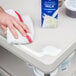 A hand cleaning up spilled milk on a gray Metro utility cart.