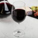 A Spiegelau Vino Grande Bordeaux wine glass filled with red wine next to a bottle of cheese and a bunch of grapes.