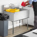 A man in a black shirt and apron pouring water into a Steelton stainless steel utility sink.