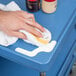 A person cleaning a blue Metro utility cart with a towel.