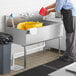 A person in a black apron pouring water into a Steelton commercial utility sink.