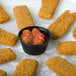 A plate of fried fish sticks with a Solo black polystyrene portion cup of sauce on the side.