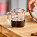 A hand using a Cambro clear polycarbonate measuring cup to measure dark liquid.