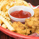 A translucent Solo souffle cup with chicken and french fries in it with a bowl of ketchup.