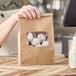 A person holding a brown Kraft paper bag with a clear window filled with cookies.