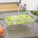 A person in a white shirt using a Rubbermaid clear colander to drain vegetables.