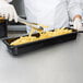 A person using tongs to put french fries into a Rubbermaid black plastic food pan.