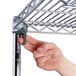 A hand using a screw to attach a metal shelf to a Metro Chrome Wire Shelving unit.