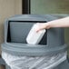 A hand throwing a white container into a grey trash can.