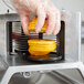 A person in gloves uses a Vollrath scalloped blade to slice oranges.