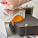 A person using a Vollrath 3/8" scalloped blade assembly to cut an orange in a machine.