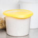 A white Rubbermaid polyethylene food storage container with a yellow lid.