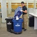 A man using a black Rubbermaid tandem dolly to move a blue trash can.