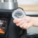 A hand holding a clear plastic lid over a clear glass jar on a counter.