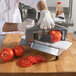 A person using a Nemco tomato slicer to cut tomatoes on a cutting board.