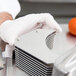 A person in white gloves using a Nemco tomato slicer to cut a tomato.