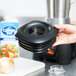 A hand holding a black lid with a hole in the middle over a Waring blender jar.