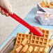 A person using a red Cambro scallop grip tong to hold a waffle.