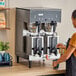 A woman using a Bunn dual coffee machine on a counter in a coffee shop.