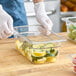 A gloved hand prepares food in a Cambro clear plastic food container.
