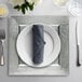 A silver Charge It by Jay plastic charger plate with silverware on a table.