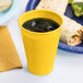 A yellow Creative Converting plastic cup filled with liquid on a table next to a plate of food.