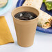 A Creative Converting Glittering Gold plastic cup filled with a drink on a table next to a plate of food.