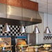 A Hanson Heat Lamps ceiling mount heat lamp with a chrome finish above a large metal container of food.