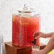 A person pouring a drink from an Acopa glass beverage dispenser.