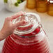 A person using a Replacement Lid for an Acopa glass beverage dispenser to pour red liquid into a glass jar.