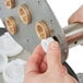 A hand using a white plastic tool to hold a white round bearing shaft.