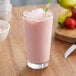 A glass of pink Big Train Strawberry Banana Frappe with a straw on a table.