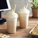 Two cups of Big Train Vanilla Latte Blended Ice Coffee with whipped cream and cookies on a table.