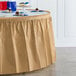 A table with a Creative Converting glittering gold plastic table skirt and plates of cupcakes.