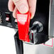 A person's finger pressing a red button on a Bloomfield automatic coffee brewer.