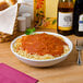 A Tuxton white porcelain serving bowl filled with spaghetti and sauce on a table with wine bottles.