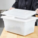 A woman holding a Carlisle white plastic container with lid on a wood surface.