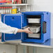 A person in a white shirt and blue chef's jacket opening a Cambro navy blue front loading insulated food pan carrier.