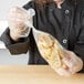 A woman in a chef's uniform holding a LK Packaging plastic food bag full of bread.