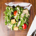 A salad with tomatoes, lettuce, and dressing on a Fineline clear plastic salad plate.