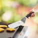 A hand using a Mercer Culinary Millennia® turner to cut a cheeseburger.