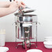 A person using a ladle to pour soup into a Vollrath steel chafing dish.