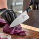 A Mercer Culinary M24106PL 6-inch Deba utility knife being used to cut a head of purple cabbage on a wooden cutting board.