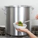 A person using a spoon to serve food from a Vollrath Wear-Ever stock pot.