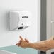 A man using a white American Dryer hand dryer on a white wall.