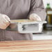 A person in a chef's uniform holding a Vollrath stainless steel pan of food.