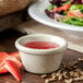 A Carlisle bone ramekin filled with strawberry sauce next to a salad.