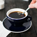 A hand holding a spoon in a CAC blue cup of coffee.