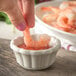 A person dipping a shrimp into a Carlisle ivory ramekin full of sauce.